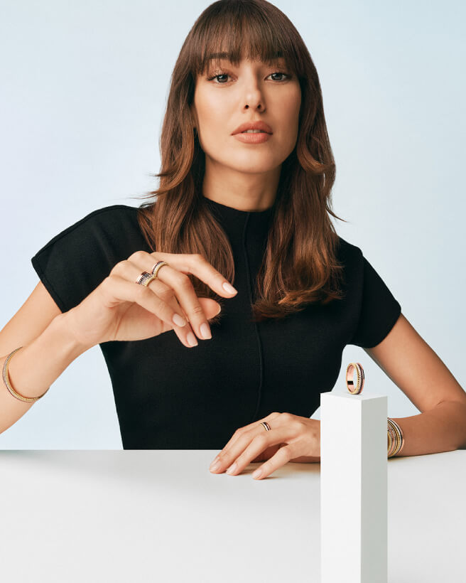 Zdjęcie modelki na zielonym tle, która podpiera głowę dłońmi i prezentuje pierścionki, bransoletki oraz kolczyki z kolekcji Quatre